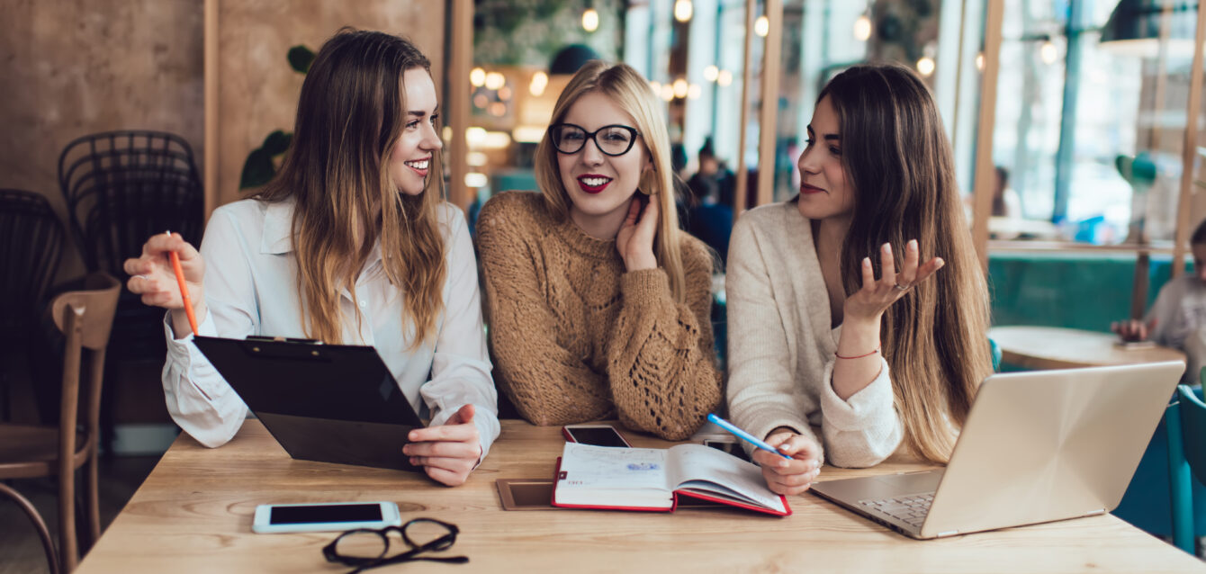 Group of smiling female friends working in cafe